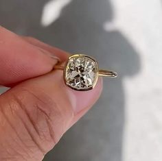 a hand holding a yellow gold ring with a diamond in it's center and the shadow of a person behind it