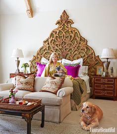 a woman sitting on a couch next to a dog in front of a large headboard