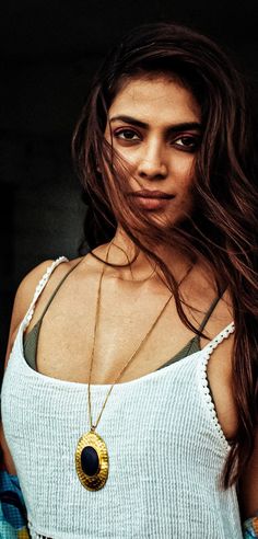 a woman with long brown hair wearing a white tank top and gold pendant necklace on her neck