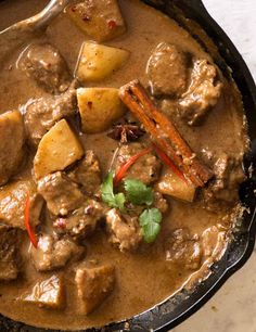 a skillet filled with meat and potatoes covered in gravy, garnished with cilantro