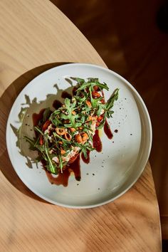 a white plate topped with vegetables and sauce on top of a wooden table next to a cup