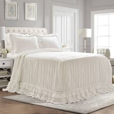 a white bed with ruffled bedspread and pillows on top of it in a bedroom