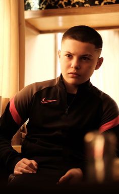 a young man sitting in front of a window wearing a black and red shirt with the word nike on it