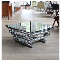 a glass and chrome coffee table in the middle of a room with chairs around it