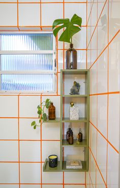 a bathroom with orange and white tiles on the walls, shelves holding various items such as plants