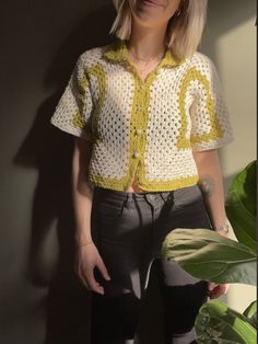 a woman standing in front of a plant wearing a yellow and white crochet top