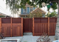 a wooden fence in front of a house with a tree and trash can on the sidewalk