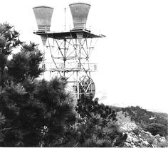 an old black and white photo of two lights on top of a tower with pine trees in the foreground