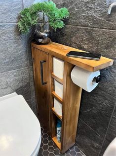 a bathroom with a toilet and a wooden cabinet in it's corner next to a plant