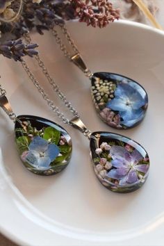 three necklaces with flowers on them sitting on a white plate next to a purple flower