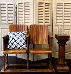 two wooden chairs sitting next to each other in front of white shuttered doors and windows