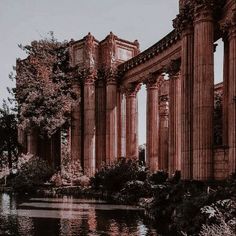 an old building with columns next to a body of water in front of trees and bushes