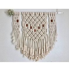 a white wall hanging with tassels and beads on the bottom, in front of a white wall