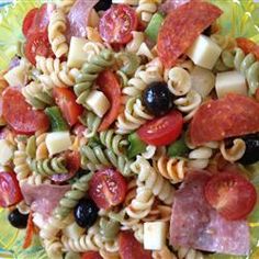 pasta salad with tomatoes, olives, and ham on a yellow glass platter