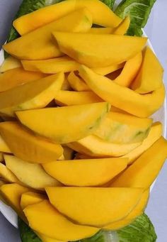 a white plate topped with sliced mangoes on top of lettuce