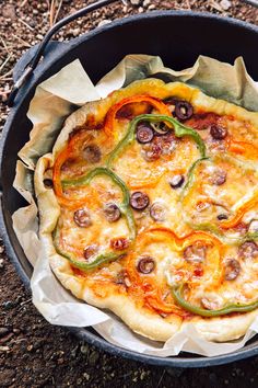 a pizza sitting in a pan on top of a dirt ground next to some grass