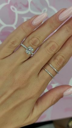 a woman's hand with pink manicured nails and three diamond rings on it