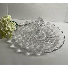 a clear glass dish with a flower on the side and a white vase behind it