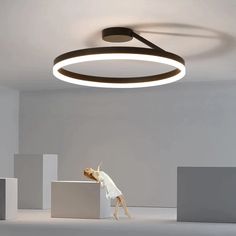 a woman standing on top of a white block in an empty room next to a circular light fixture