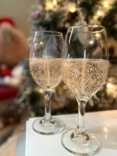 two wine glasses sitting next to each other on a counter top near a christmas tree