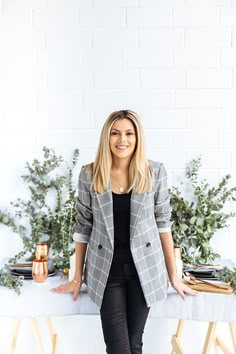 a woman standing in front of a table with candles and greenery on the side