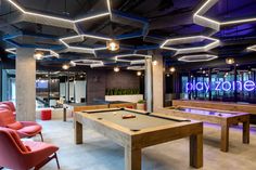 a pool table and chairs in a room with neon lights hanging from the ceiling above it