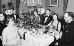 a group of people sitting around a table with halloween decorations on it's head