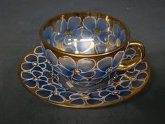 a tea cup and saucer decorated with blue flowers on a gold rimmed saucer