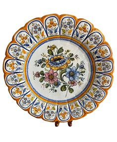 an orange and blue plate with flowers painted on the side, sitting in front of a white background