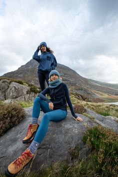 two women sitting on top of a large rock