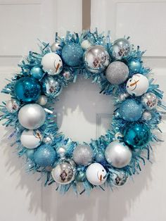 a blue and silver christmas wreath hanging on the front door with ornaments in different colors