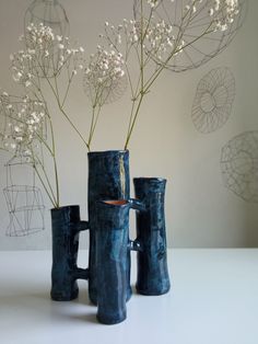 three blue vases with white flowers in them on a table next to a wire sculpture