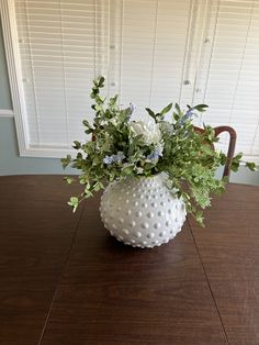 a white vase filled with flowers on top of a wooden table