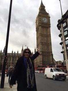 a woman standing on the side of a road in front of a clock tower with her arms up