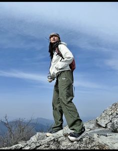 a man standing on top of a rocky hill next to a blue sky and clouds