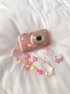 a pink camera sitting on top of a white bed next to a necklace and bracelet