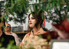 a woman with red lipstick standing next to two men in front of some plants and trees