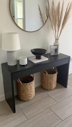 a black console table with two baskets under it and a round mirror on the wall