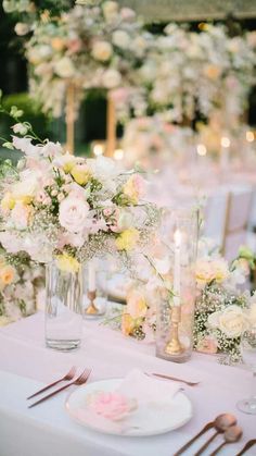 the table is set with white and pink flowers in vases, silverware, and candles