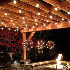 an outdoor dining area is lit up with string lights and hanging globes over the fire pit