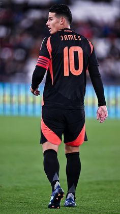 a soccer player in black and orange uniform walking on the field with his foot up