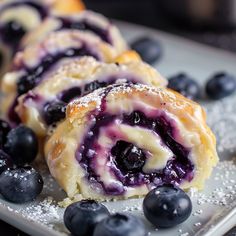 blueberry pastry rolls on a plate with powdered sugar and fresh blueberries around them