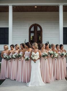 a group of bridesmaids standing in front of a white house with their bouquets