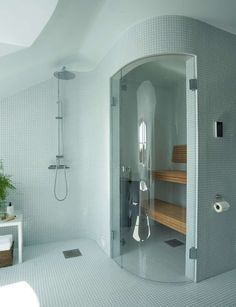 a white tiled bathroom with a walk in shower next to a wooden bench and potted plant