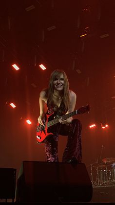 a woman playing guitar on stage with red lights in the backgroung behind her