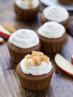 cupcakes with white frosting and apple slices on a wooden table next to sliced apples