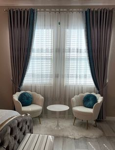 two white chairs sitting next to each other in front of a window with drapes