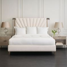 a large white bed sitting on top of a hard wood floor next to two lamps