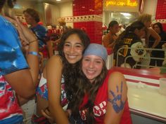 two girls are posing for the camera in front of some food court seating and fans