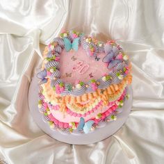 a heart shaped cake on top of a white tablecloth with butterflies and ribbons around it